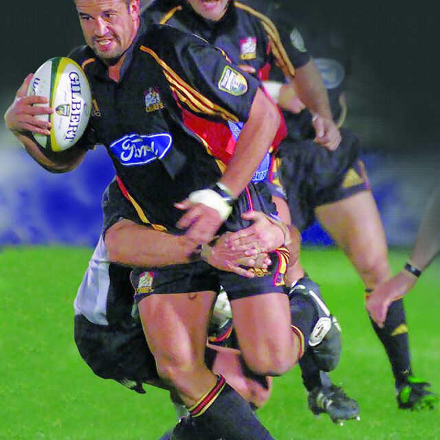 Chiefs player breaks a tackle while running the ball during a night match.