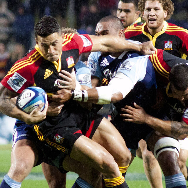 Chiefs player fends off opponents while carrying the ball strongly in a high-intensity match.