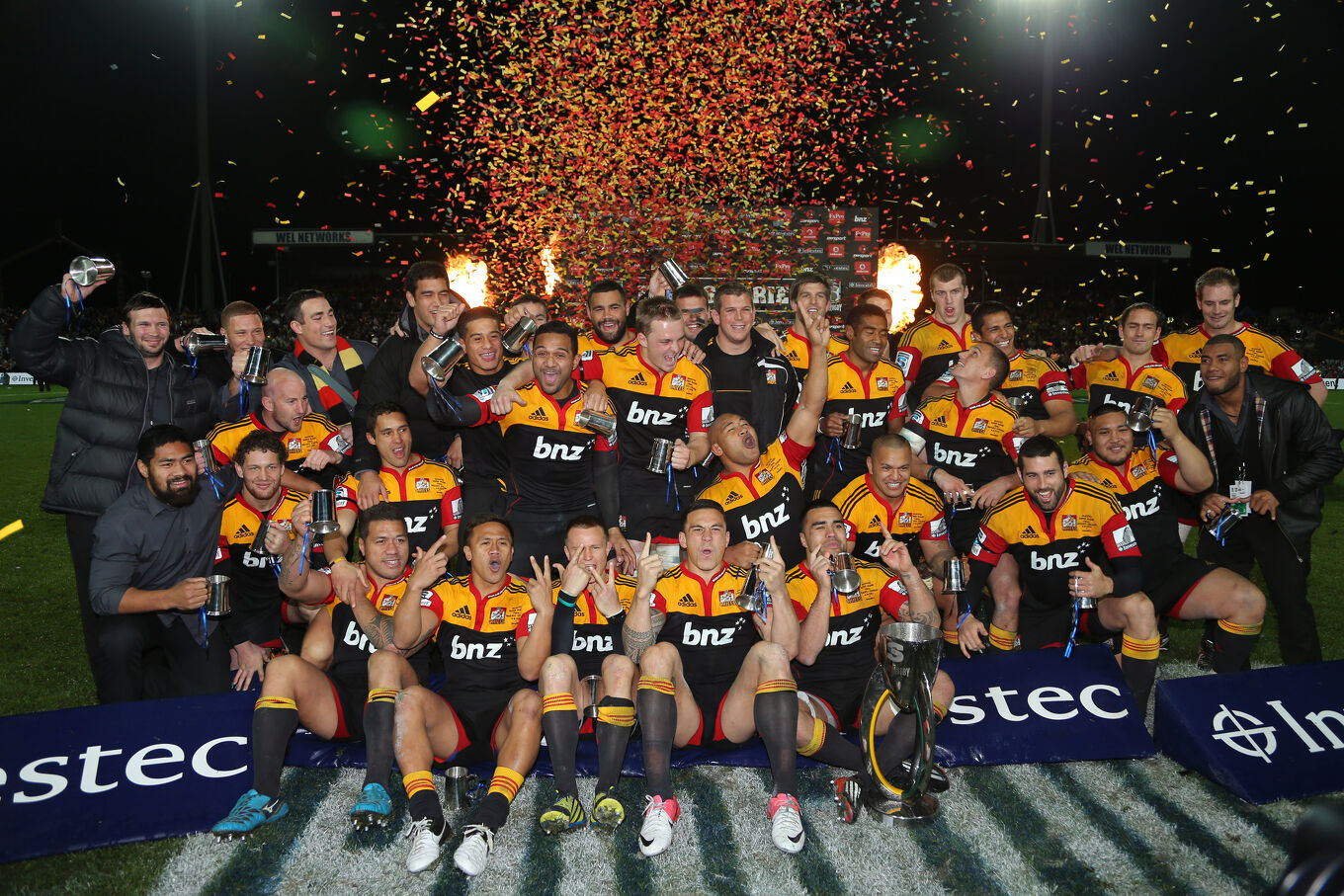 Chiefs players celebrate a championship victory with the trophy on the field under confetti and lights.