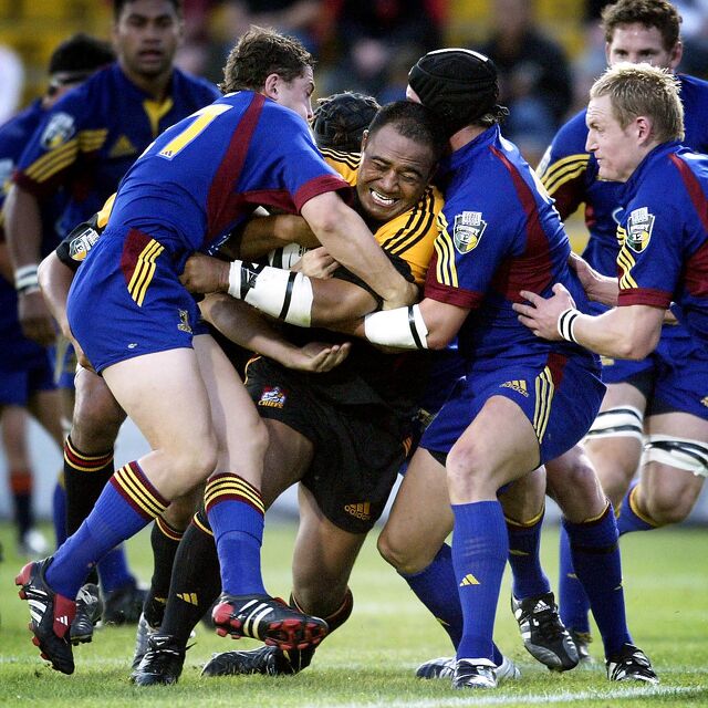 Chiefs player takes on multiple Highlanders defenders in a physical tackle contest.